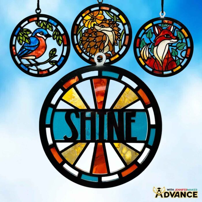 Four Alcohol Ink Paper Stained Glass window projects featuring a bird, hedgehog, "shine," and fox designs, hanging against a bright blue sky with fluffy clouds