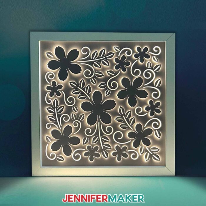 An illuminated Backlit Shadow Box shines in a dark room, with an intricate 3D floral design cut into its layers