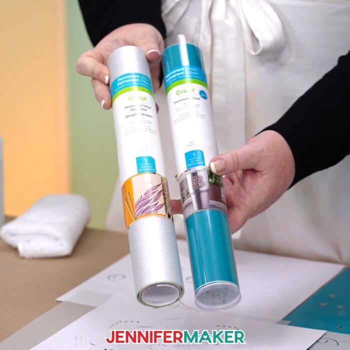 Hands hold a roll of silver shimmer adhesive vinyl and a roll of plain teal adhesive vinyl to be used in making a Backlit Shadow Box