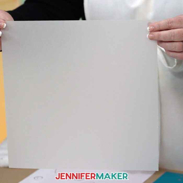 Hands hold up a piece of optional white vellum used to soften the light from inside of a Backlit Shadow Box craft