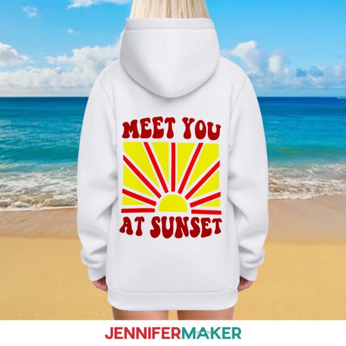 A person facing away from the camera wearing a white hoodie with a vinyl design on the back reading "meet you at sunset" with a yellow and orange sun in the middle.