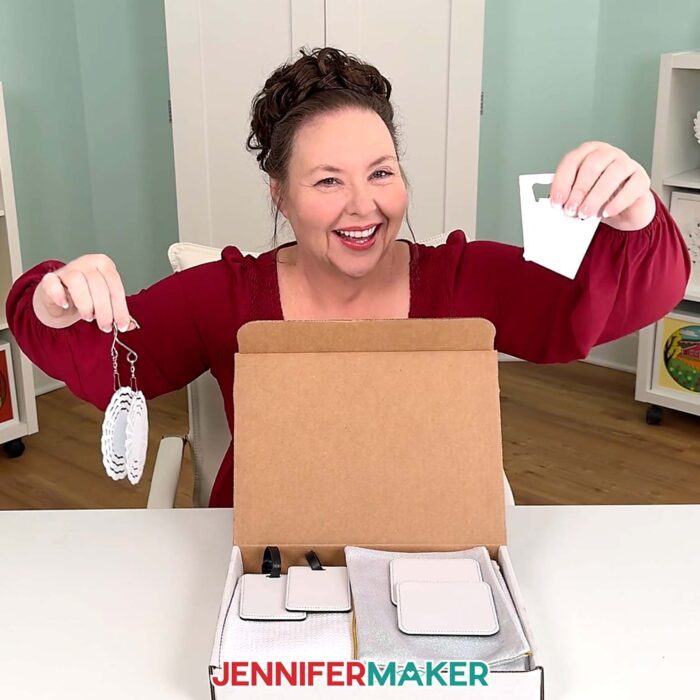 Jennifer holds up the bottle openers and mini wind spinners from the Beginner Sublimation Kit with the box displayed one the table in front of her