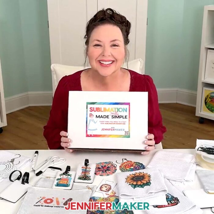 Jennifer smiles and holds the Beginner Sublimation Kit with the contents displayed one the table in front of her