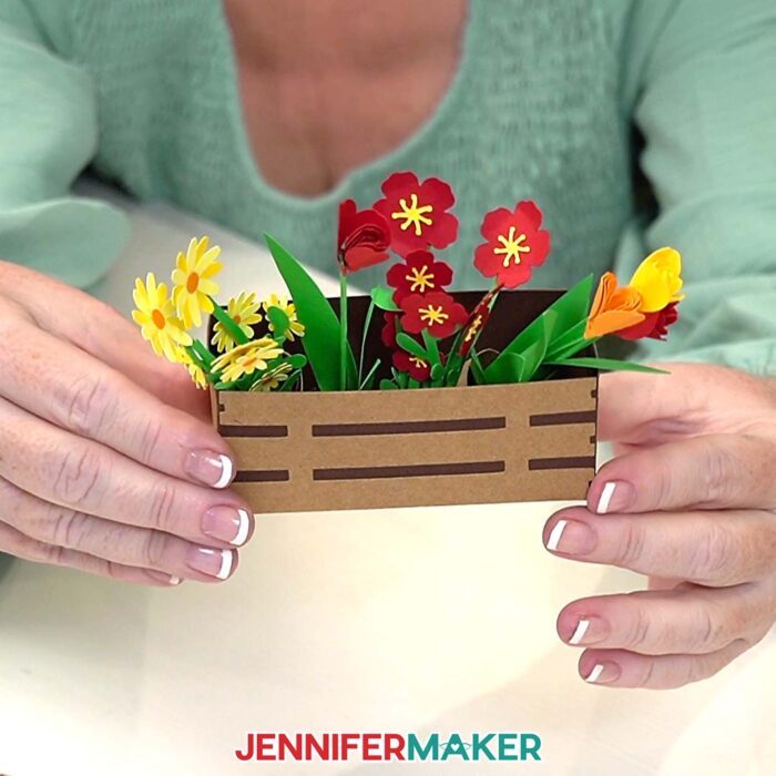 Jennifer holds up mini paper flowers in a 3D planter held together with craft glue