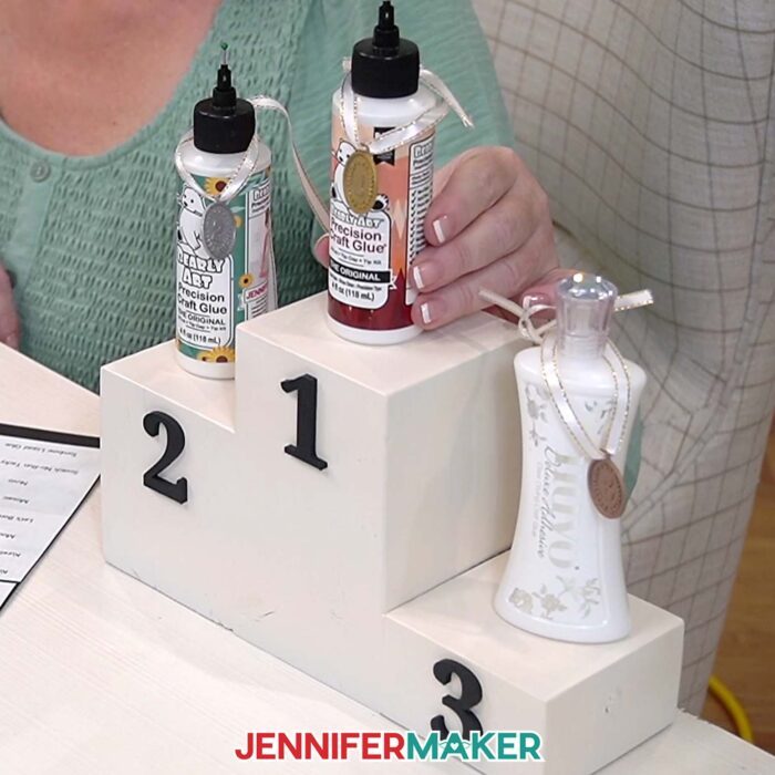 Jennifer's three Best Craft Glues on a ranking pedestal: #1 is a new bottle of Bearly Art, #2 is a two-year old bottle of Bearly Art, and #3 is a bottle of Nuvo Deluxe Adhesive.
