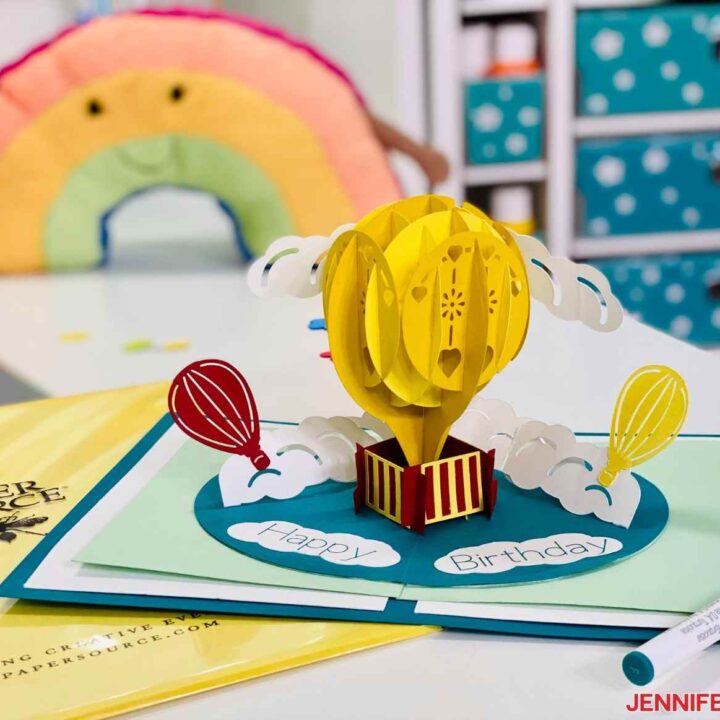 Colorful open hot air balloon birthday card pop up design on a desk.