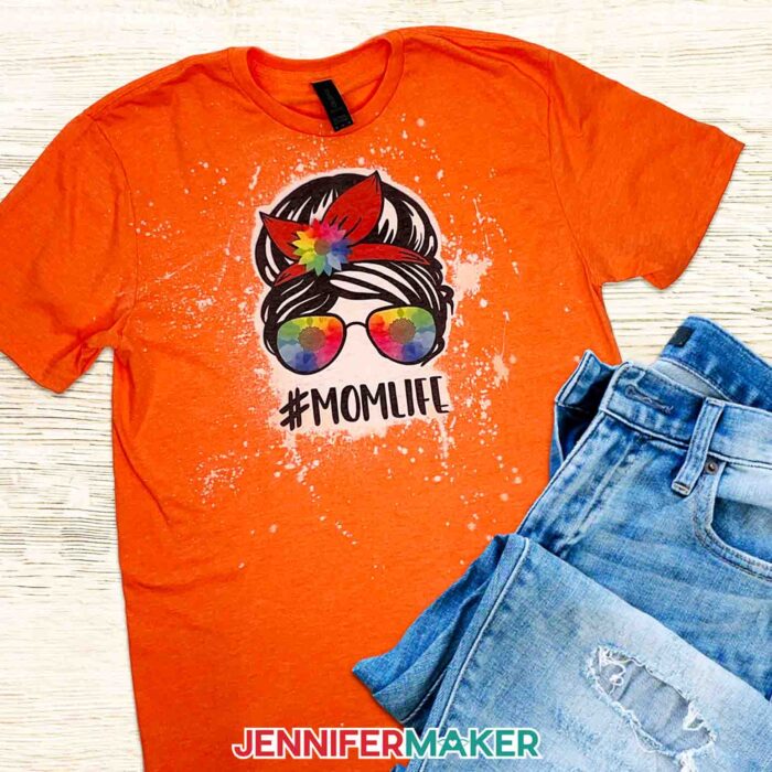 Orange bleached and sublimated shirt with "#MOMLIFE" design, styled with jeans. Learn all about bleaching shirts for sublimation with JenniferMaker's new tutorial!