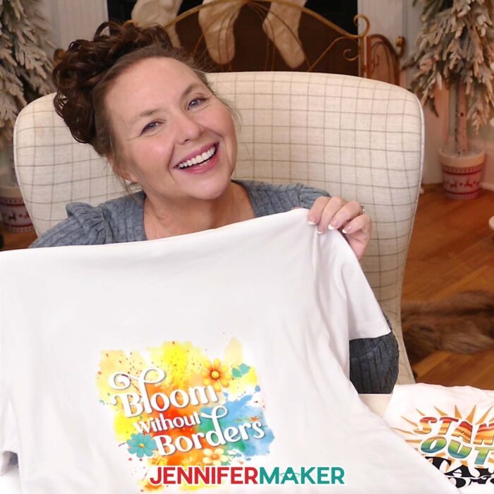 Jennifer holds up a custom version of her "Bloom Without Borders" T-shirt, featuring pretty flowers placed around the lettering.