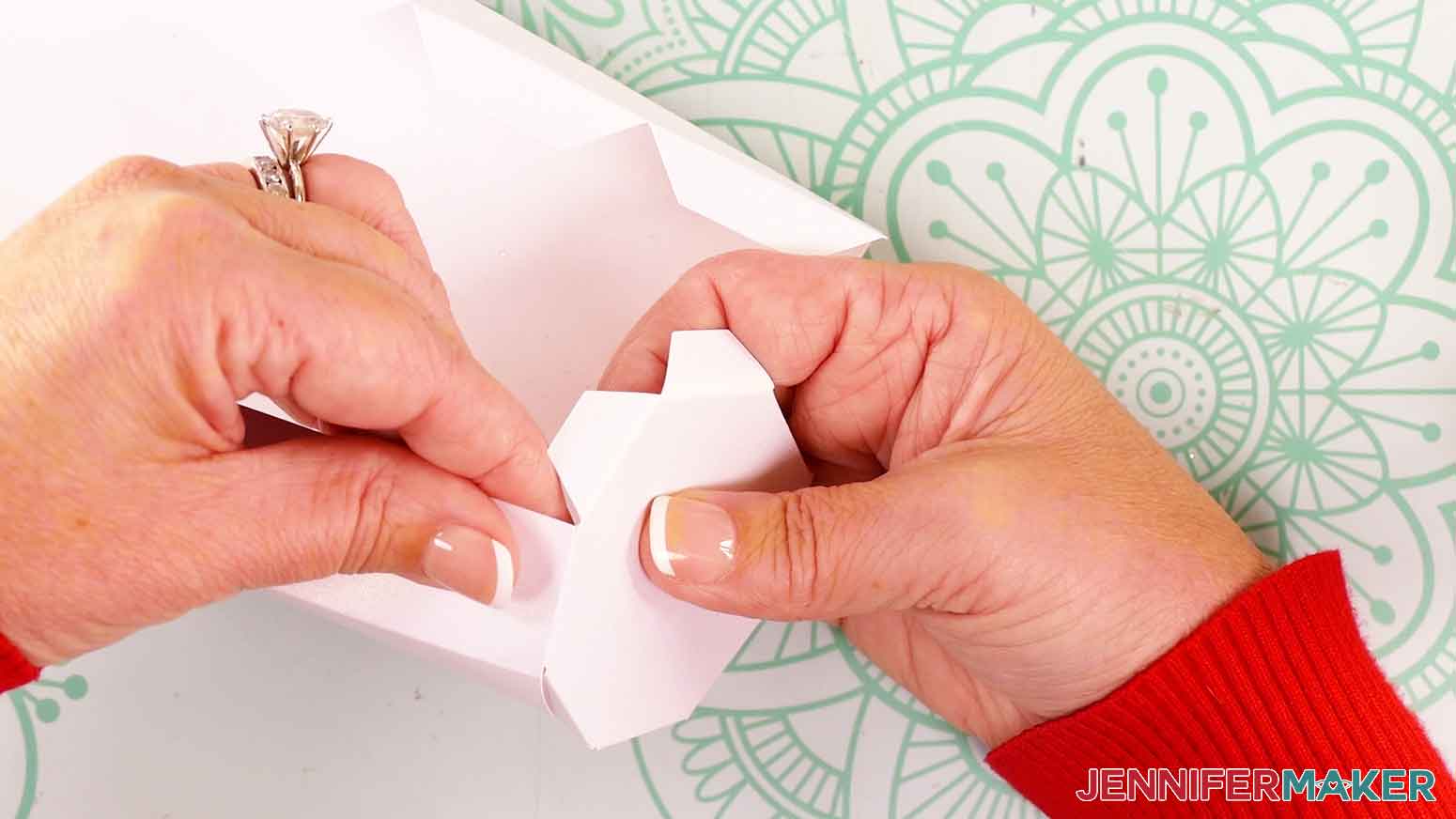Starting at the end without the tabs, press the glued tab from the base piece onto the bottom of the first folded panel.