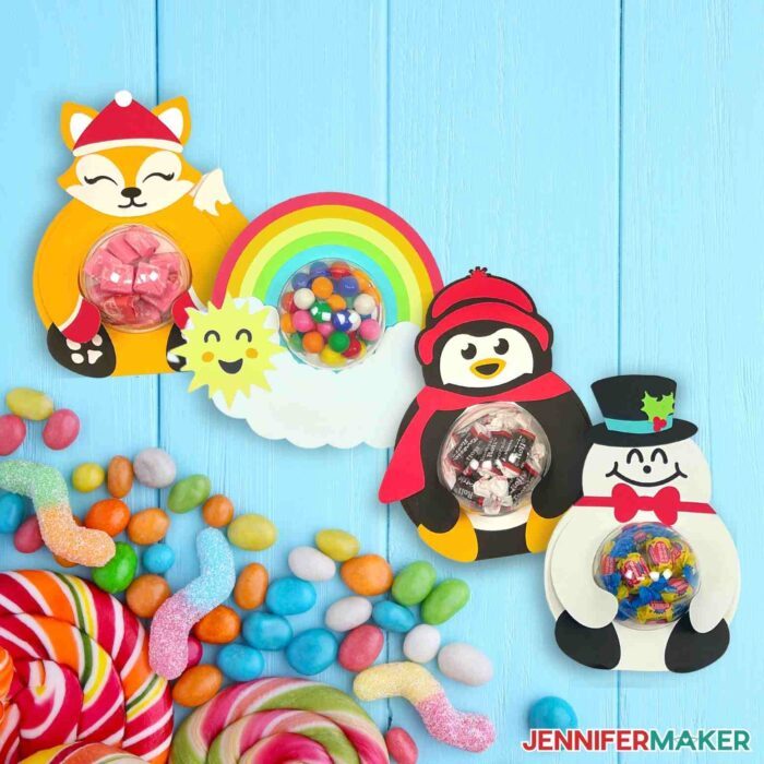 Fox, rainbow, snowman, and penguin candy holders on a blue background next to candy