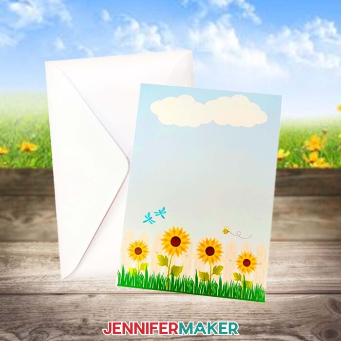A note card with sunflowers printed on the front floats against a clear blue sky, with a coordinating white envelope. Learn to make your own with the How To Make Cards In Canva tutorial