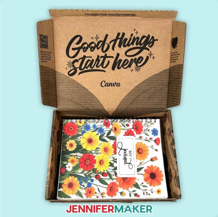 A custom journal made in Canva sits in a shipping box that says "Good things start here. Canva." The journal's cover has "My Journal" written on an background of red, yellow, orange, and blue wildflowers.