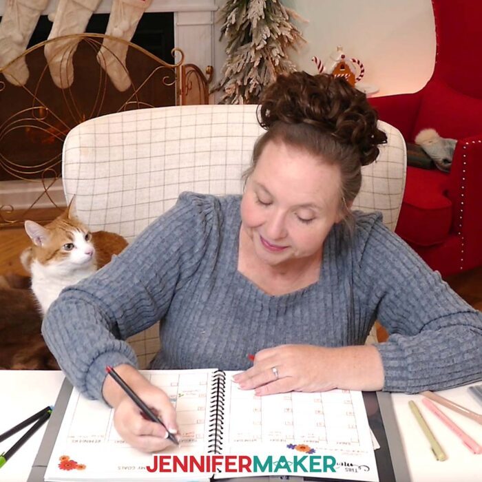 Jennifer writes in the journal she created using Canva while her cat Butterscotch watches over her shoulder.