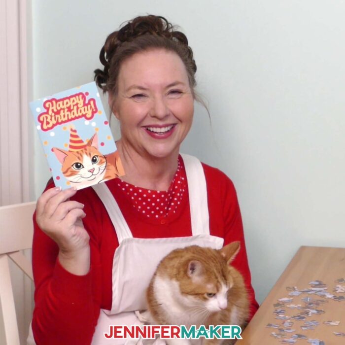 Jennifer holds up a Happy Birthday card with her cat Butterscotch's face on it while Butterscotch sits in her lap