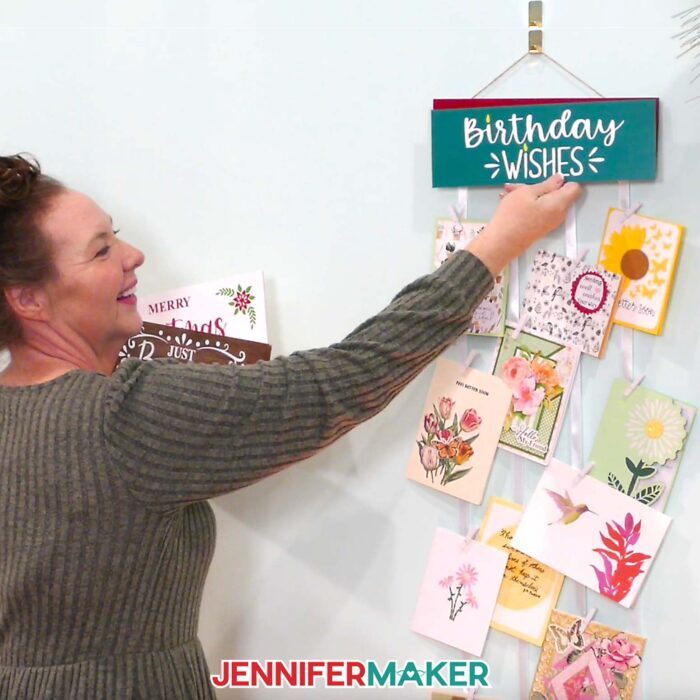 Jennifer swaps her interchangeable greeting card hanger's display panel with a teal and white "Birthday Wishes" panel.