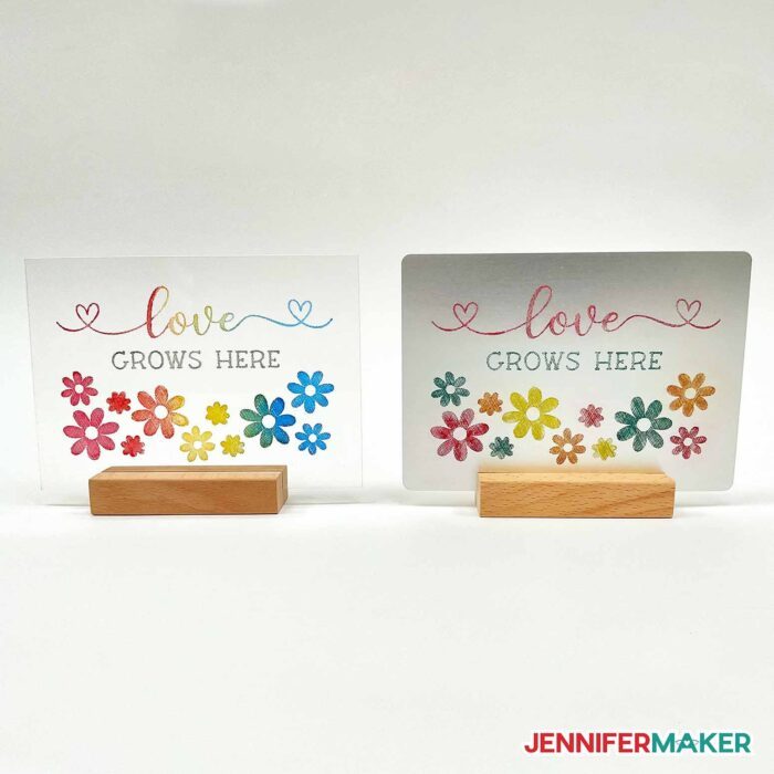 Comparison of acrylic ink color engraving Love Grows Here design on a clear acrylic plaque and metal version in wooden stands.