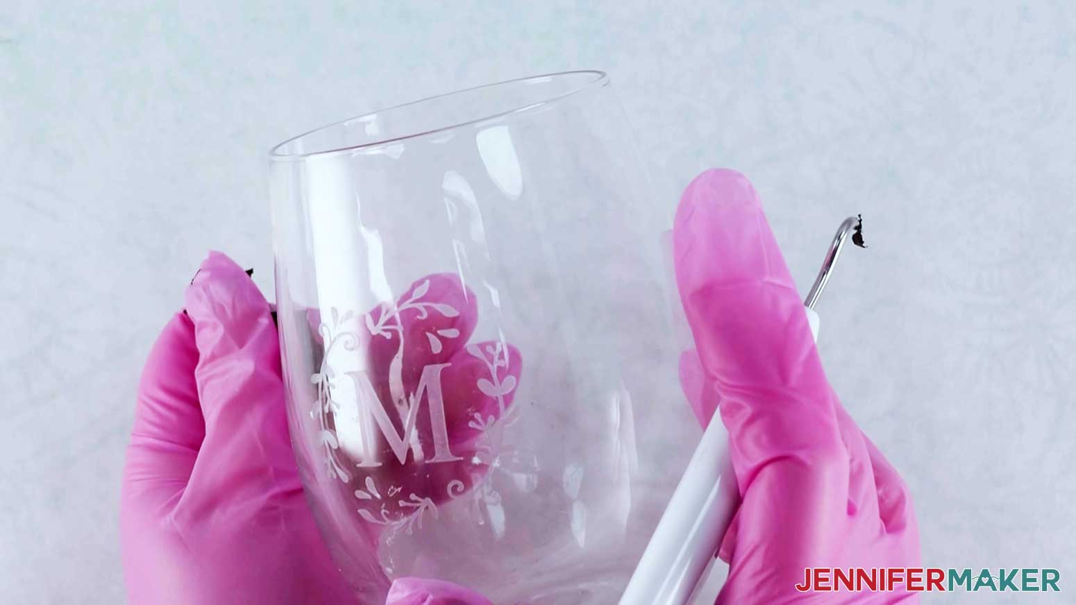 A photo showing two hands with gloves on holding a wine glass with the color glass etching design etched in the center, the letter M clearly visible