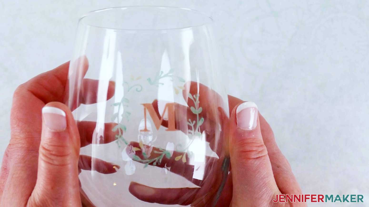A photo showing two hands holding a wine glass with the color glass etching design etched in the center and colored with red, green, and yellow paint