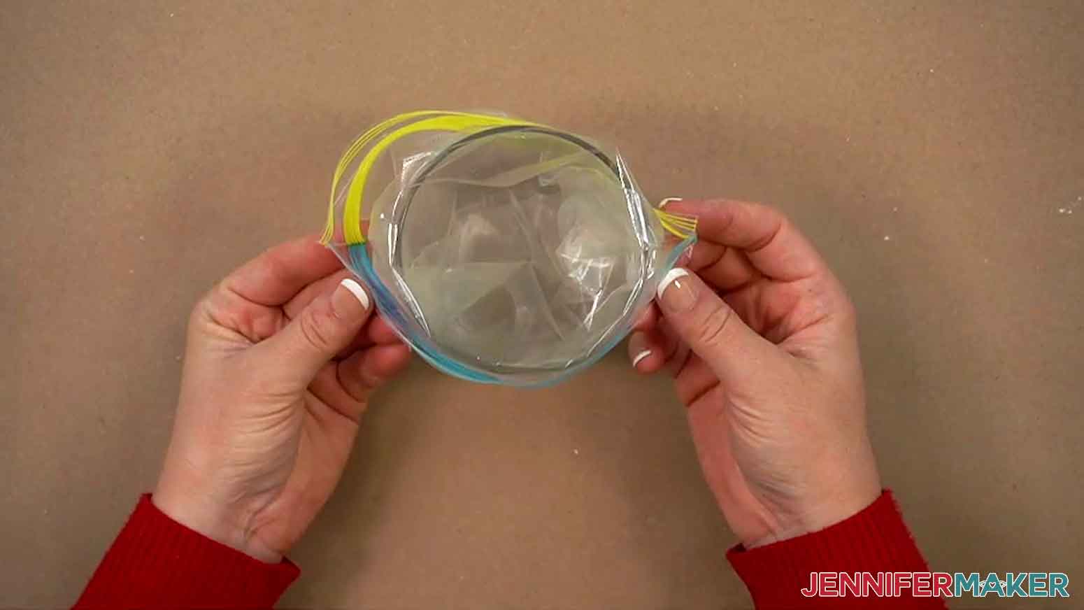 A ziploc baggie is being placed in a tall glass with the top edge of the baggie folded down over the top rim of the glass.