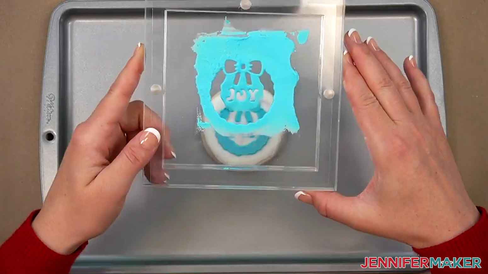 The excess icing and stencil inside the stencil holder are lifted straight up off the cookie.