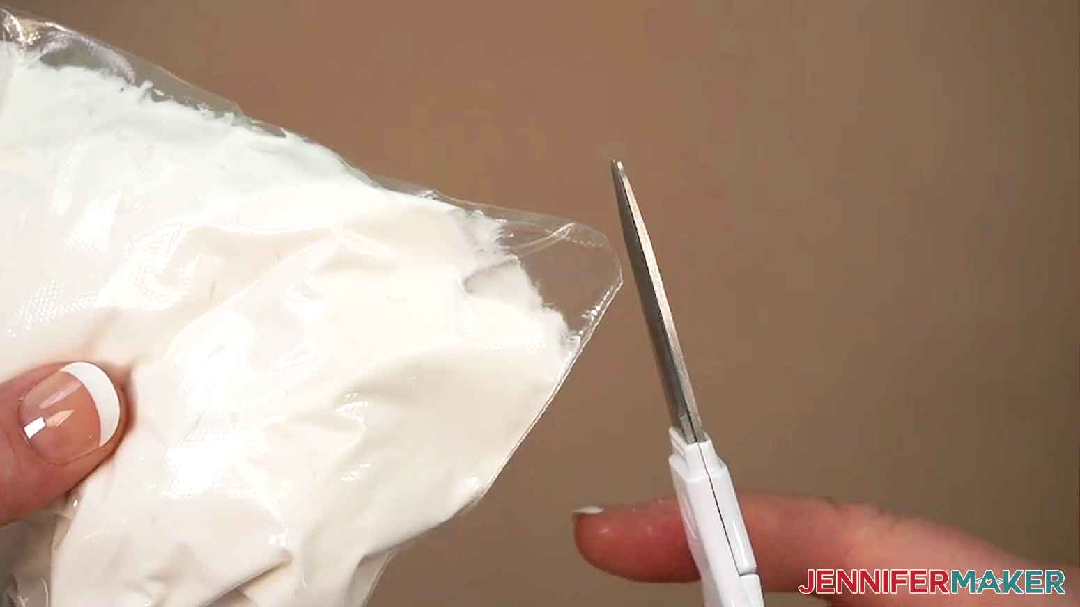 The sandwich baggie has been filled with icing and one of the corners of the baggie is being snipped with scissors.