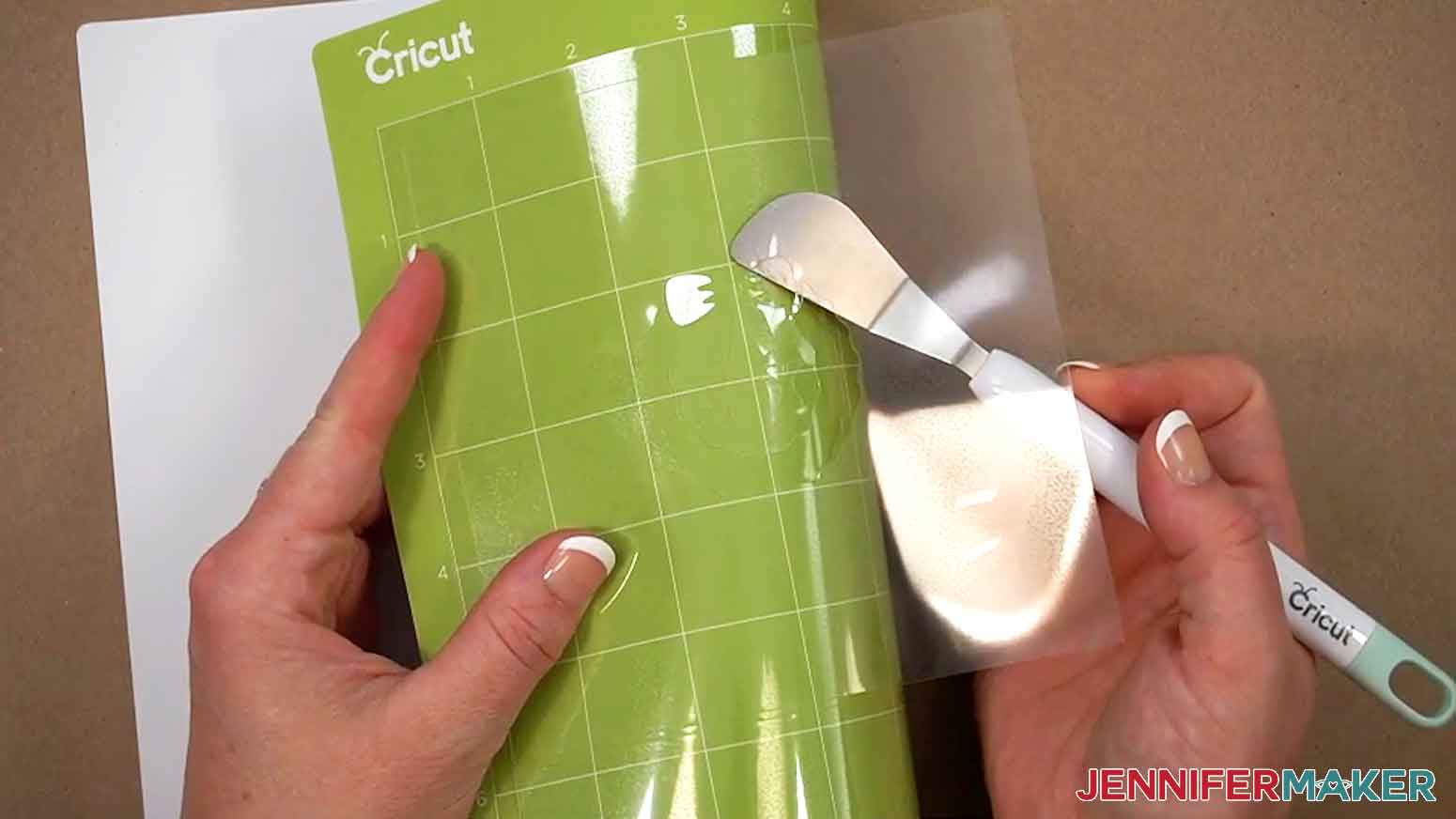 A small spatula is being used to lift the mylar cookie stencils gently off the green standard grip mat.