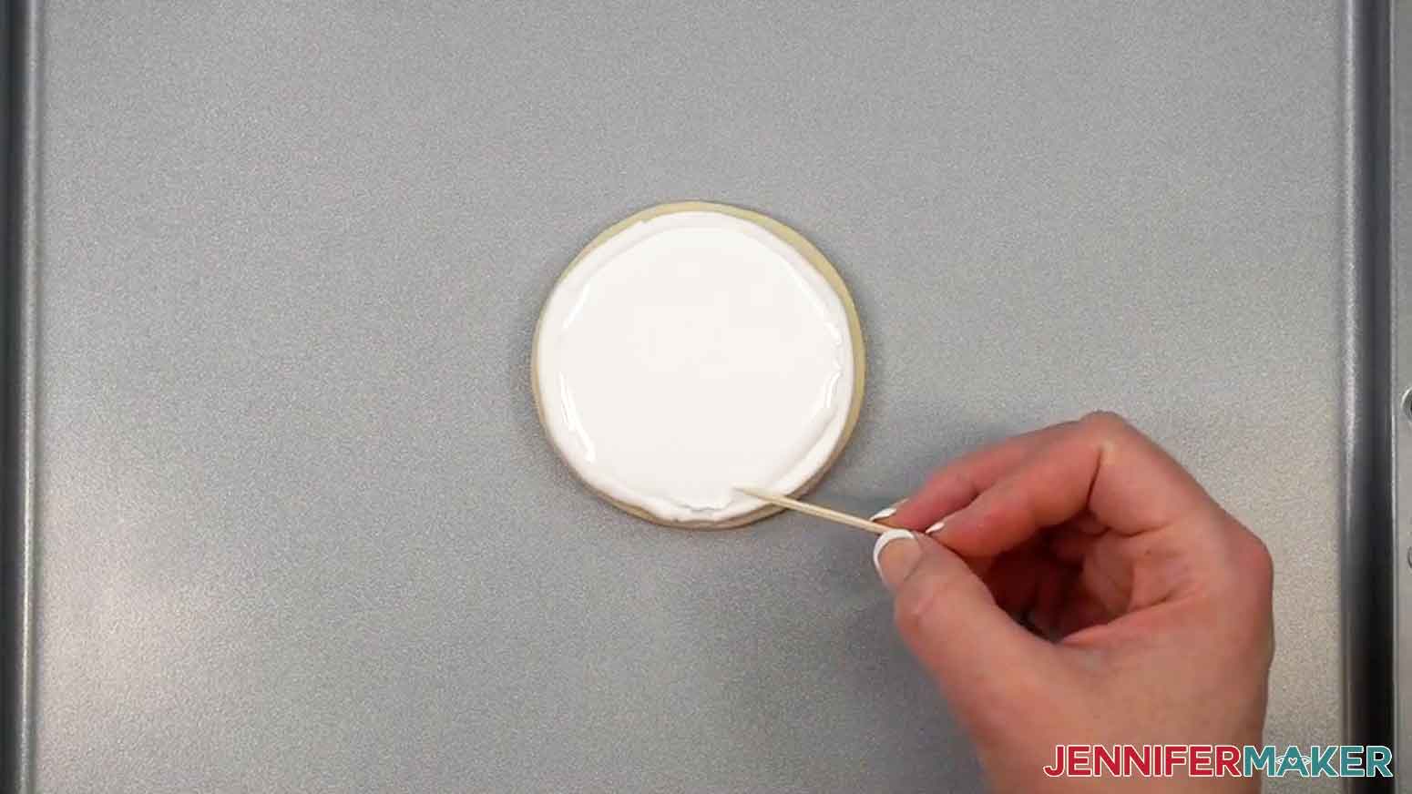 A toothpick is being used to spread the icing on the cookie.