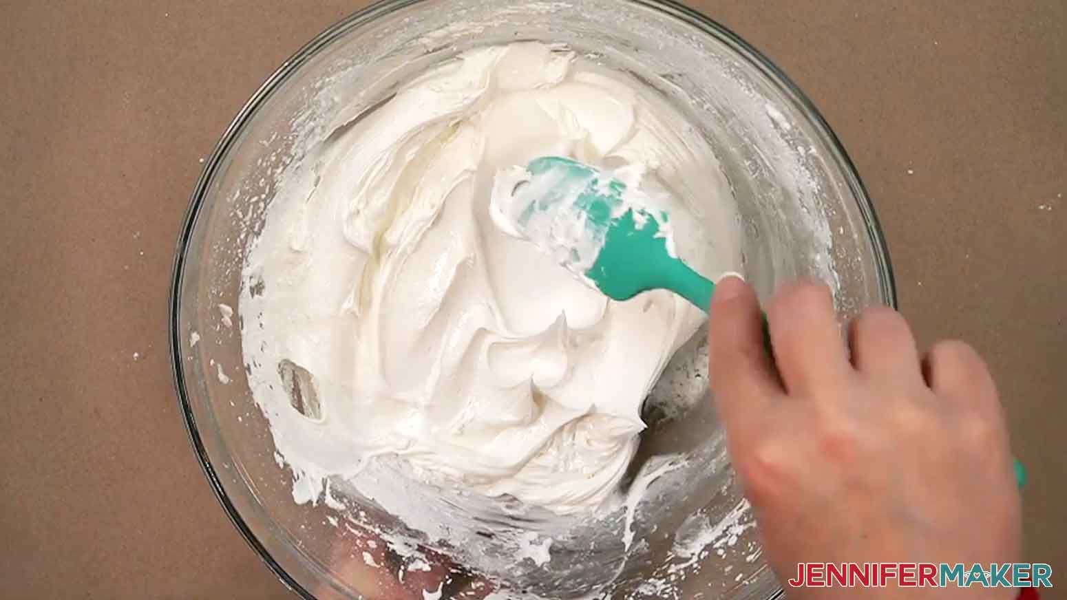 A spatula is used to mix the icing and the icing drips off the spatula forming stiff peaks in the bowl.