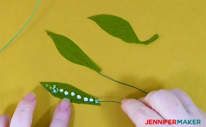Gluing wire to the underside of a crepe paper leaf