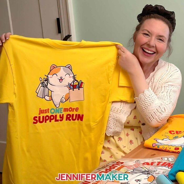 Jennifer Maker shows off a T-shirt decorated with one the Cricut DTF Transfers she ordered from Cricut Design Space, featuring a cute crafting cat design