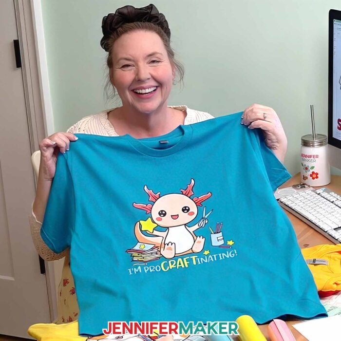 Jennifer Maker shows off a T-shirt decorated with one the Cricut DTF Transfers she ordered from Cricut Design Space, featuring a cute crafting axolotyl design