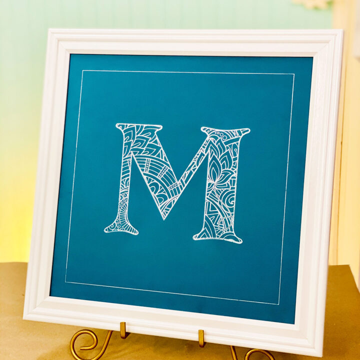 Beautiful foil mandala letter in silver foil on blue cardstock with a white frame