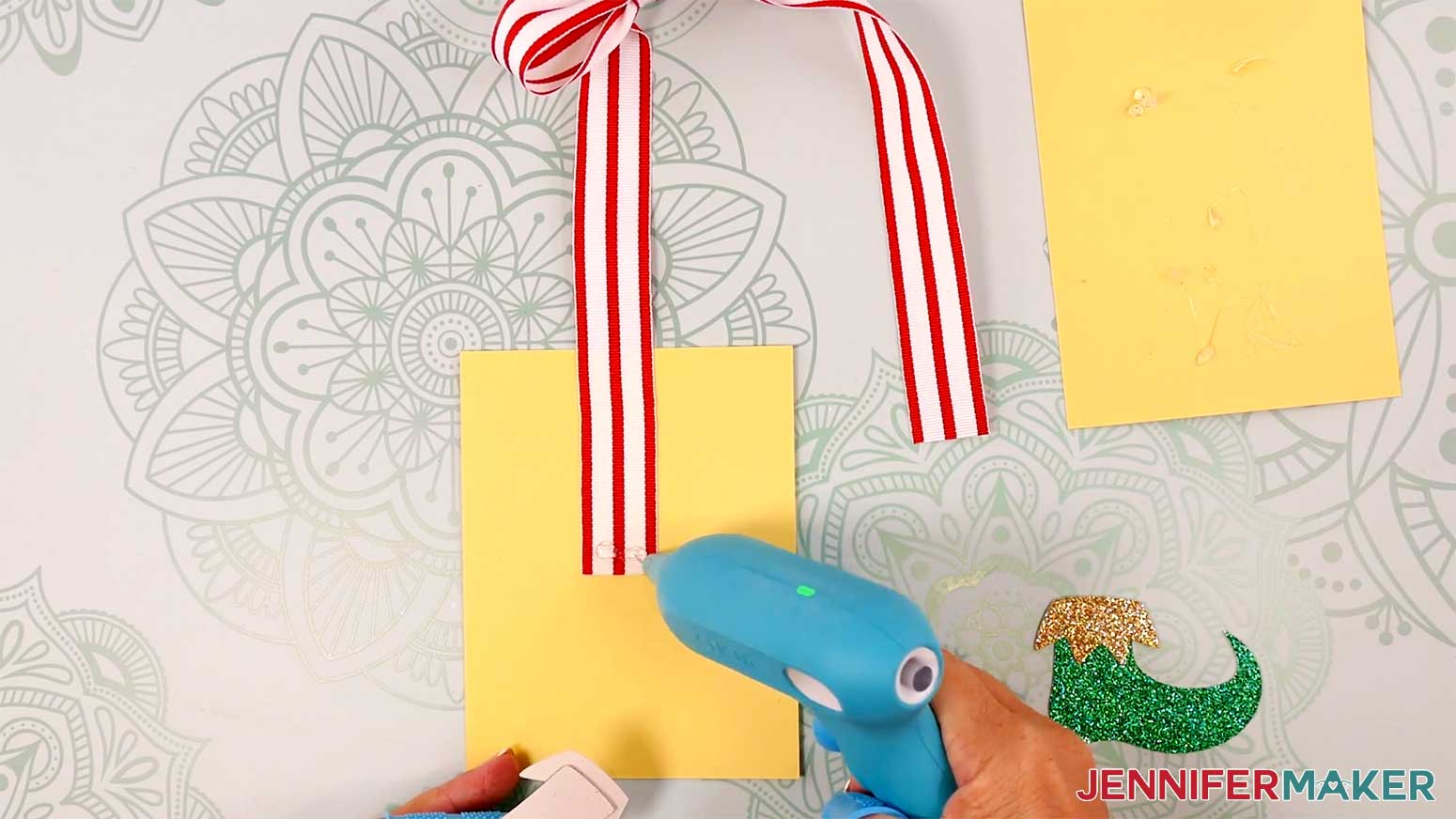Apply hot glue to the front end of the ribbon's tails Apply hot glue to the top front of the boots pieces for the Elf Boots Ribbon in the Cricut Gift Wrapping Ideas project.