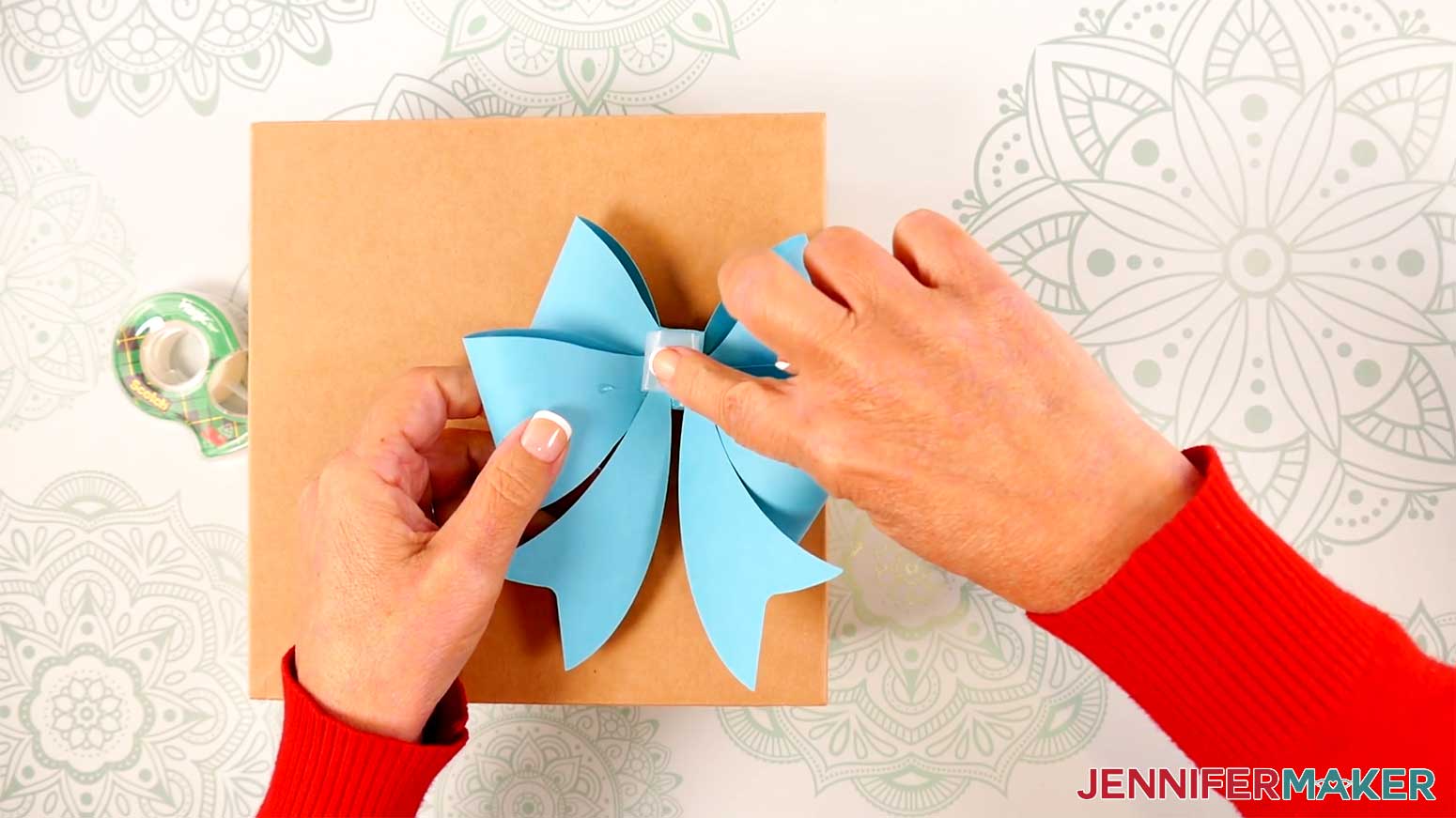 Adhere a rolled up piece of clear tape to the back of the Fancy Paper Bow to a wrapped gift in the Cricut Gift Wrapping Ideas project.