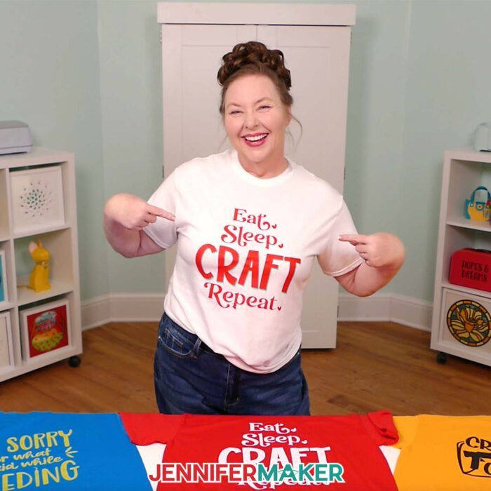 Jennifer Maker wears a white T-shirt she decorated with iron-on vinyl to say "Eat, Sleep, Craft, Repeat" and points to the design. Learn how to make your own in the Cricut Iron-On Vinyl Tutorial