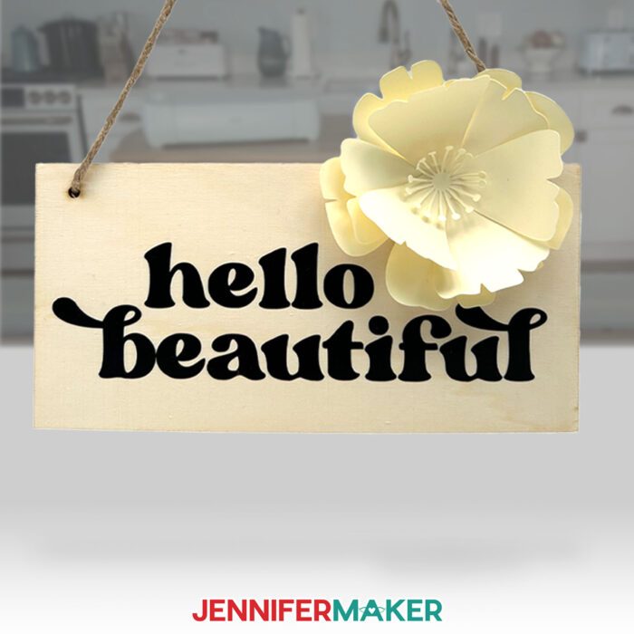 A wooden sign decorated with vinyl reading "hello beautiful," with a cream colored paper flower attached, made with the bonus materials included with the new Cricut Maker 4 & Cricut Explore 4!