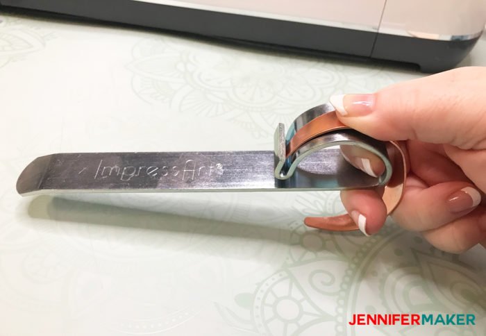 Using an ImpressArt bracelet bending bar to bend a copper bracelet that's been engraved on the Cricut