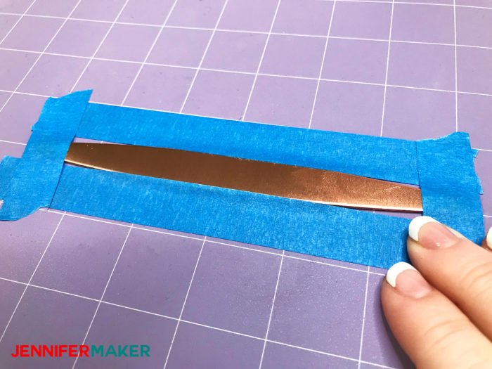 Taping a copper bracelet to a purple Cricut StrongGrip Mat to keep it from moving when we use the Cricut Maker Engraving Tool