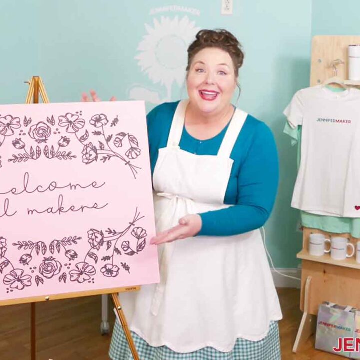 Jennifer Maker with a 24" x 28" pink cardstock sign that reads "Welcome Makers" drawn using the Cricut large format cutting machine.