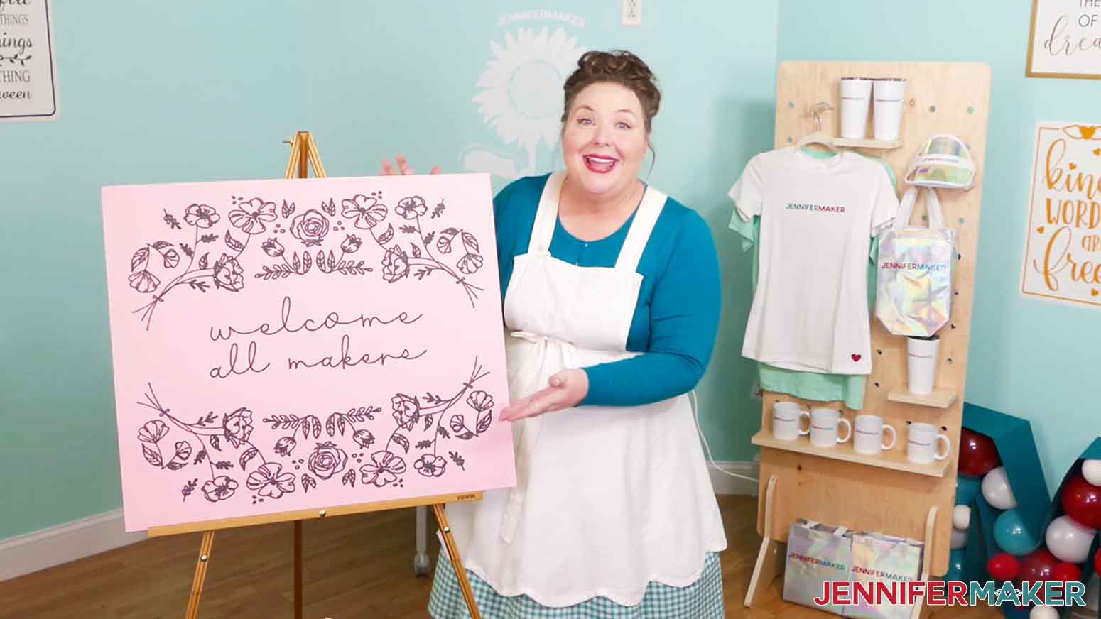 Jennifer Maker with a 24" x 28" pink cardstock sign that reads "Welcome Makers" drawn using the Cricut large format cutting machine.