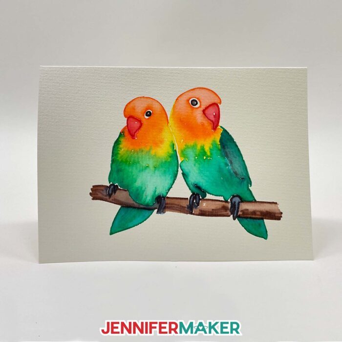A DIY watercolor card featuring two lovebirds made with Cricut watercolor markers.