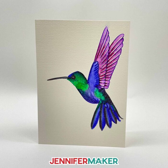 A DIY watercolor card featuring a hummingbird made with Cricut watercolor markers.