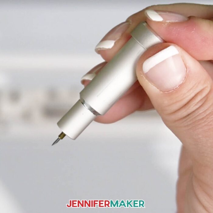 Hand pushing the plunger down on a Cricut blade housing, pushing the blade out. Learn how to replace a Cricut blade with Jennifer Maker's new tutorial!