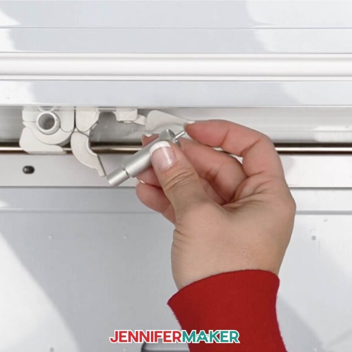 Hand removing the blade and blade housing from a Cricut cutting machine. Learn how to replace a Cricut blade with Jennifer Maker's new tutorial!