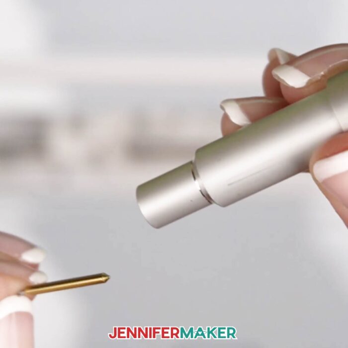 Person holding a Cricut blade housing in one hand, blade in the other, after just pulling the blade out from the housing. Learn how to replace a Cricut blade with Jennifer Maker's new tutorial!