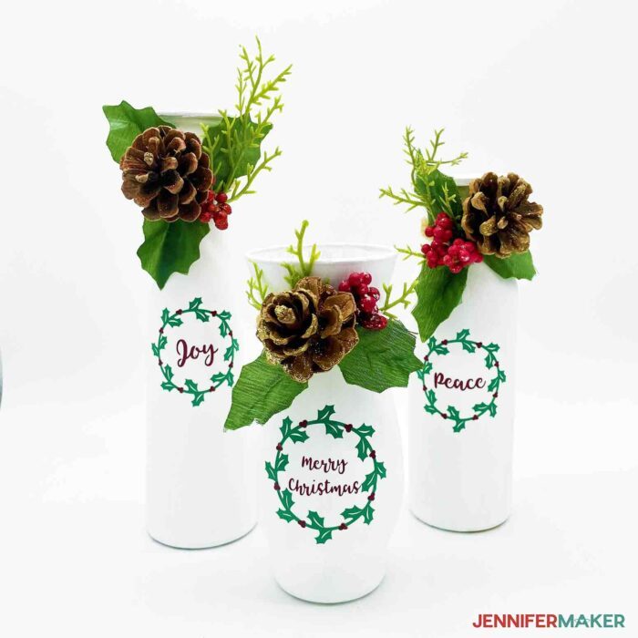 Painted vases with holiday sentiments and pinecones using vinyl for DIY Christmas decorations.