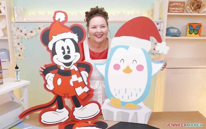 Jennifer Maker holding DIY cut out characters of Santa Mickey and a cartoon Christmas penguin in craft room