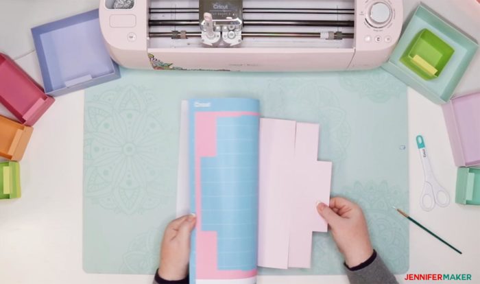 Gently peeling a cutting mat away from a piece of pink cardstock that has been cut on a Cricut to make a DIY drawer divider to organizer a drawer