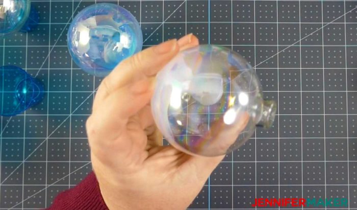 Swirling adhesive around the inside of a clear ornament to make DIY glitter ornaments