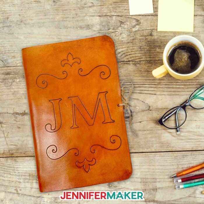 A DIY leather journal in brown with decorative engraved flourishes and the initials JM on a desk.